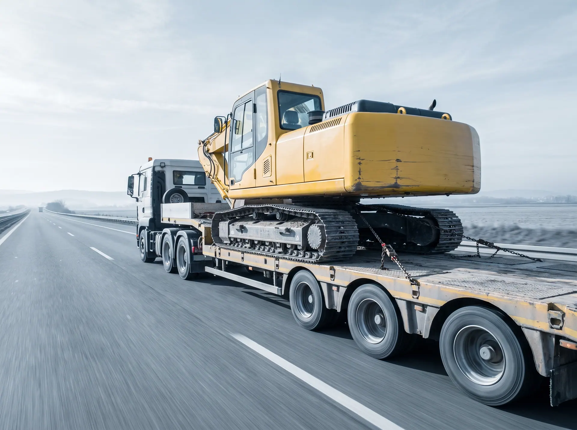 A new excavator riding a lowbed trailer along an open highway